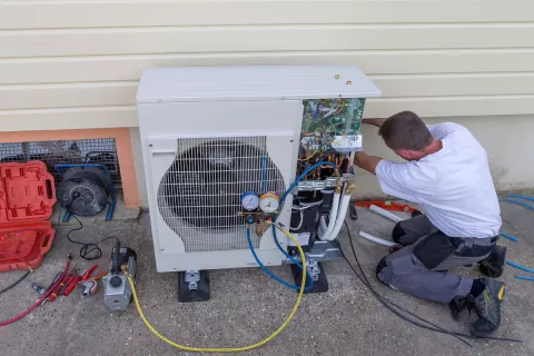 Ein Installateur schraubt an einer Wärmepumpe an der Seite von einem Haus.